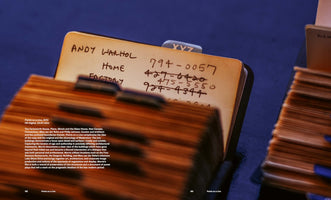 Nahaufnahme einer alten, handgeschriebenen Rolodex-Karteikarte für Andy Warhol mit den Einträgen Home und Factory sowie mehreren Telefonnummern, von denen einige durchgestrichen sind.
