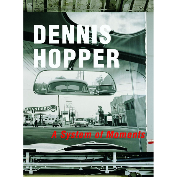 Das Buchcover für Dennis Hopper: A System of Moments zeigt eine Schwarz-Weiß-Fotografie einer amerikanischen Straßenszene, aufgenommen aus der Perspektive eines Autos, wobei der Rückspiegel im Mittelpunkt steht.