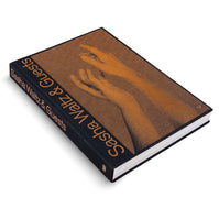 Ein schwarzes Buch mit dem Titel Sasha Waltz & Guests in orangefarbener Schrift. Auf dem Einband befindet sich eine orangefarbene Grafik von zwei Händen im Halbton-Stil. Das Buch liegt auf einem weißen Hintergrund.