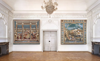 Ein großer, weißer Raum mit Stuckverzierungen, Parkettboden und einem Kristallkronleuchter. An der Rückwand hängen links und rechts einer weißen Doppeltür zwei große, moderne Wandteppiche in einem historisch anmutenden Stil. Der linke zeigt eine Szene mit Säulen und Figuren vor einer Stadtkulisse, der rechte eine Landschaft mit Burg und Regenbogen.