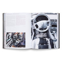 Ein aufgeschlagenes Buch, das auf der rechten Seite ein Foto des mit weißer und schwarzer Farbe bemalten Innenraums eines Autos zeigt und auf der linken Seite Text und ein kleineres Foto des Autos von außen.