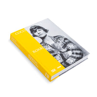 Ein gebundenes Buch mit dem Titel Coco Chanel's Roaring Twenties, das schräg auf einem weißen Hintergrund liegt. Das Cover zeigt ein Schwarz-Weiß-Foto von Coco Chanel. Der Buchrücken und eine Banderole sind leuchtend gelb.