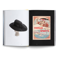 Ein aufgeschlagenes Buch. Die linke Seite zeigt einen schwarzen Hut mit breiter Krempe auf einem Mannequinkopf. Die rechte Seite zeigt ein Vintage-Plakat für Monaco Sports mit einer Frau in einem Flugzeug über einer Küstenlandschaft.