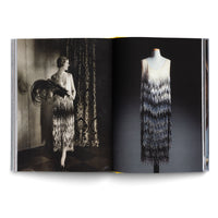 Ein aufgeschlagenes Buch zeigt auf der linken Seite eine Schwarz-Weiß-Fotografie einer Frau im Flapper-Stil der 1920er Jahre, die ein Fransenkleid, Perlen und einen Federfächer trägt. Auf der rechten Seite ist dasselbe schimmernde Fransenkleid in Farbe auf einer Schneiderpuppe vor dunklem Hintergrund abgebildet.