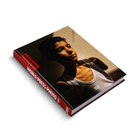 Ein schräg liegendes Hardcover-Buch mit dem Titel World Press Photo 2025. Das Coverfoto zeigt das Porträt eines Jungen in einem weißen Unterhemd, der von hartem Licht angestrahlt wird und tiefe Schatten wirft. Der Buchrücken ist rot mit weißer Schrift.