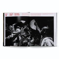 Ein aufgeschlagenes Buch mit einer großen Schwarz-Weiß-Fotografie, die eine energiegeladene Tanzszene in einem überfüllten Raum zeigt. Menschen tanzen dicht gedrängt, mit erhobenen Armen. Eine Person in der Mitte tanzt ekstatisch, während rechts jemand einen großen, geöffneten Fächer in die Luft hält.