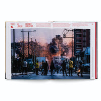 Ein aufgeschlagenes Buch zeigt auf einer Doppelseite unter der Überschrift Gaza Under Israeli Attack eine nächtliche Straßenszene, in der eine Menschenmenge die Explosion eines Gebäudes mit Rauch und Funkenregen beobachtet.