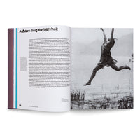 Eine aufgeschlagene Buchseite. Links befindet sich Text unter der Überschrift Auf dem Berg der Wahrheit. Rechts zeigt eine Schwarz-Weiß-Fotografie eine Person in fließender Kleidung, die mit erhobenen Armen freudig über einer Uferlandschaft in die Luft springt.