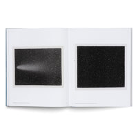 Ein aufgeschlagenes Buch zeigt auf einer Doppelseite zwei schwarz-weiße Bilder eines Sternenhimmels. Das linke Bild zeigt einen Kometen mit einem leuchtenden Schweif, während das rechte Bild nur das Sternenfeld darstellt.