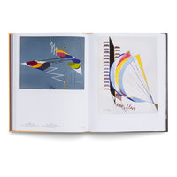 Ein aufgeschlagenes Kunstbuch liegt auf einer weißen Oberfläche und zeigt eine Doppelseite mit zwei abstrakten, farbenfrohen Kunstwerken von Sonia Delaunay. Das linke Bild hat einen blaugrauen Hintergrund, das rechte einen weißen.