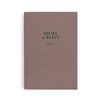 Ein Buch mit einem staubig-rosafarbenen Einband, auf dem in dunkelgrüner Schrift der Titel HILMA af KLINT und darunter Flora steht.