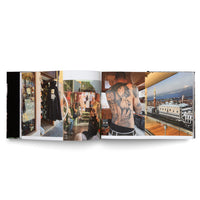 Ein aufgeschlagenes Fotobuch, das eine Doppelseite mit vier Farbfotografien zeigt: ein venezianisches Geschäft mit Masken, Menschen auf einem Boot, der Rücken eines Mannes mit einem großen Tattoo römischer Wahrzeichen und eine Luftaufnahme des Markusplatzes in Venedig.